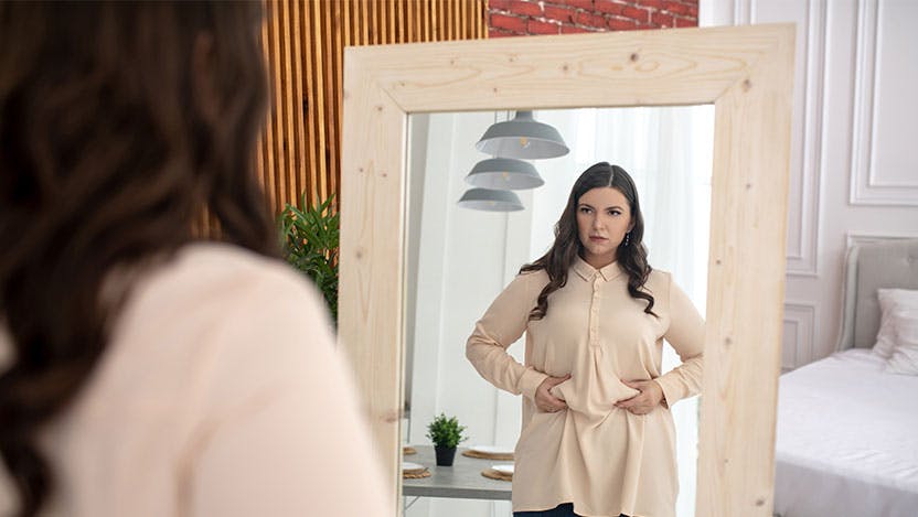 Woman in mirror squeezing menopause belly fat